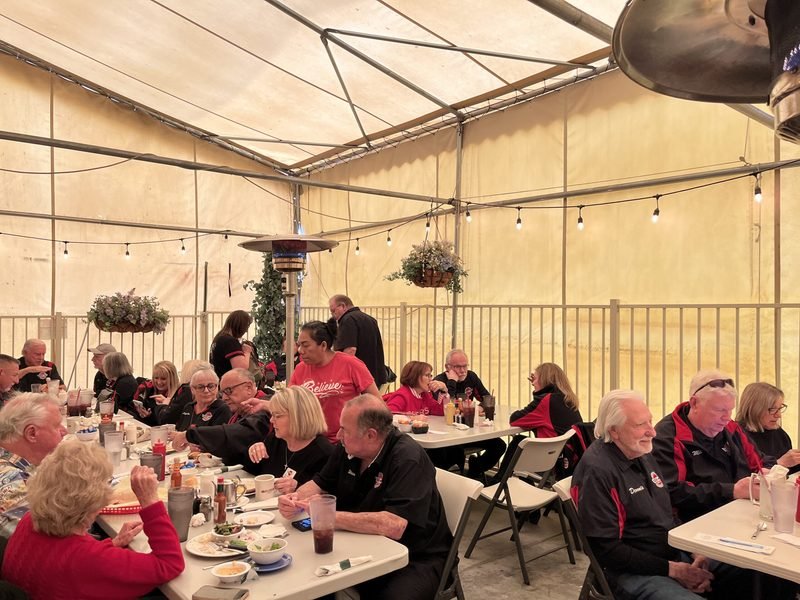 A full patio of guests dining beneath string lights