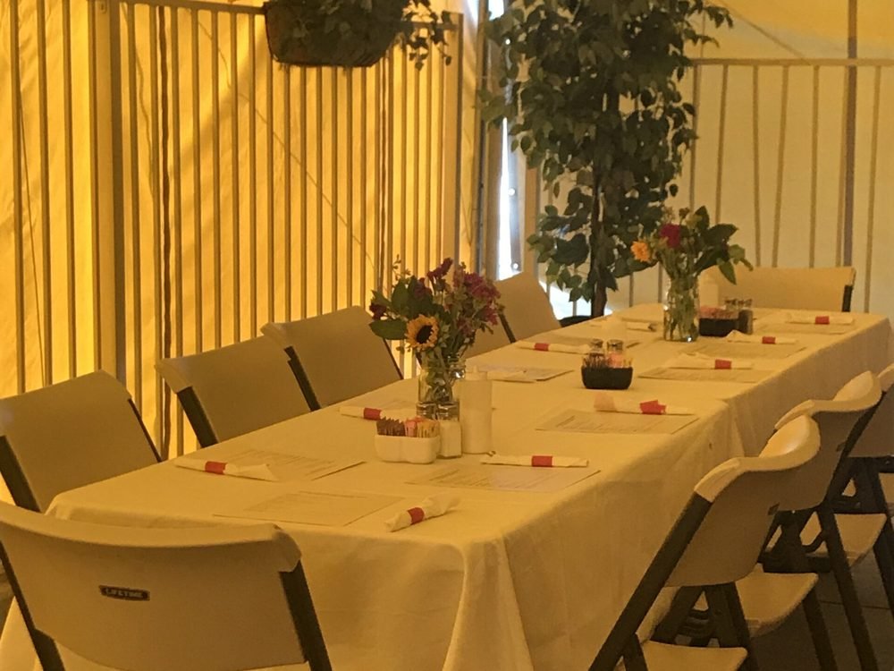 The covered and heated patio at The Red Caboose Café, long tables set with white linens and flowers under string lights
